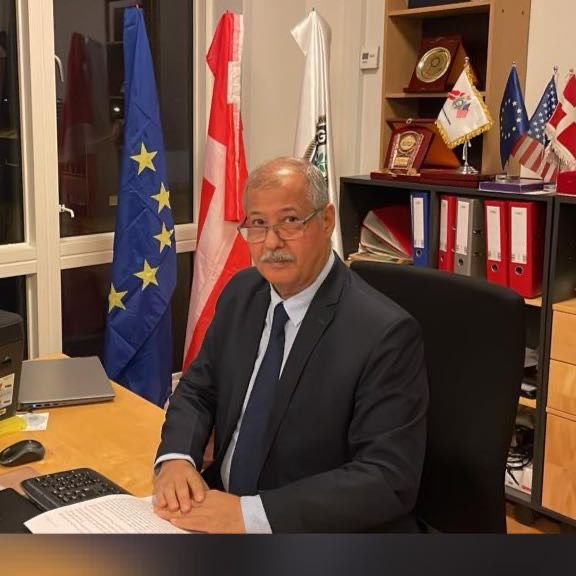 Talal Akram Al-Nadawi, President and Founder, seated at his desk with the European and Danish flags behind him